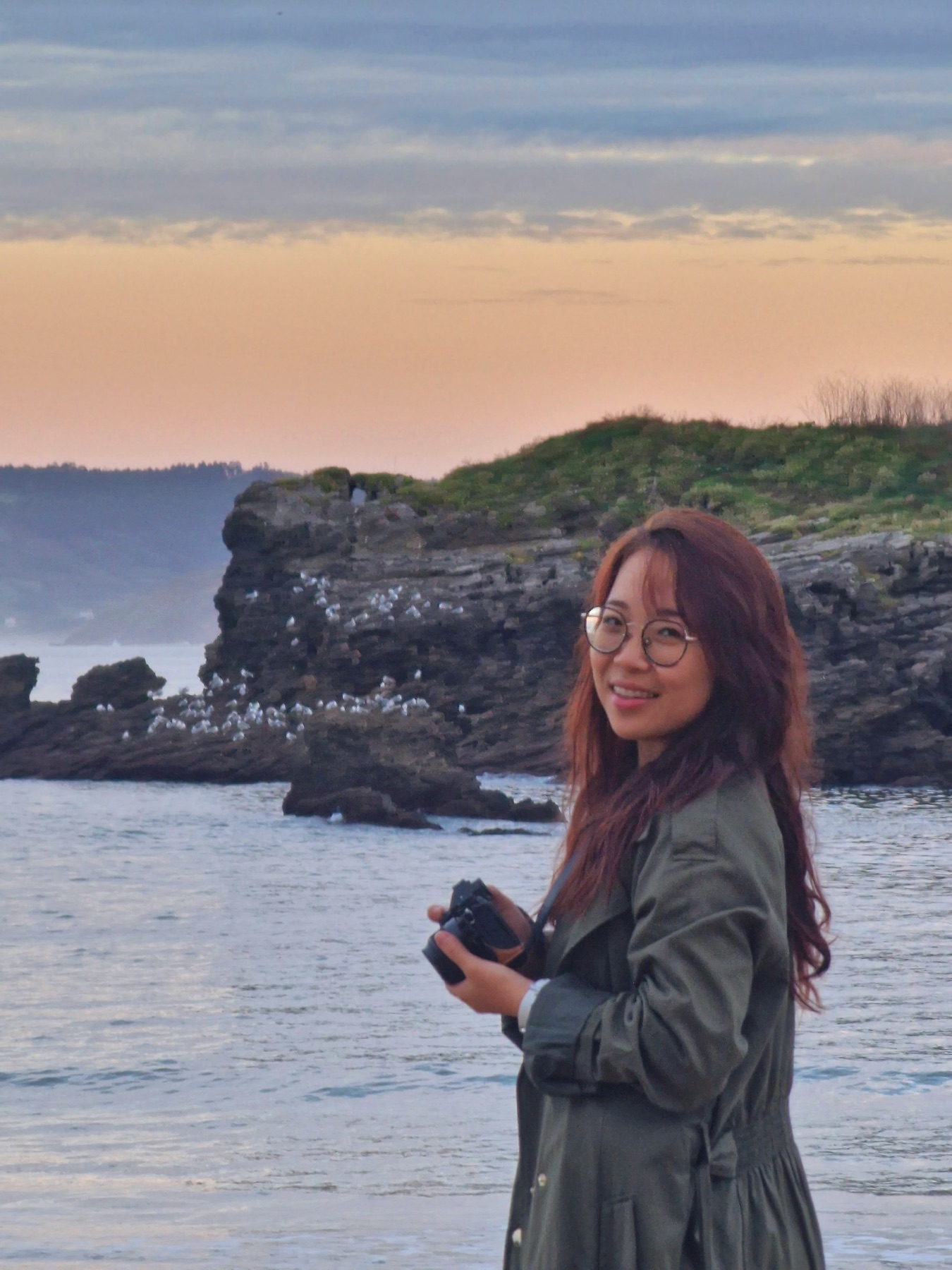 Tianyu smiling by the sea, holding a camera